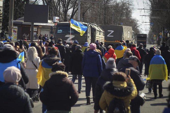 Những người dân mang cờ Ukraine đi về phía xe tải của quân đội Nga trong cuộc phản đối chống lại sự chiếm đóng của Nga ở Kherson. Ảnh: AP.